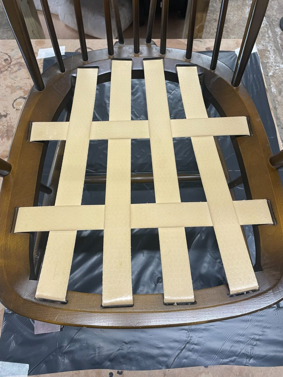 Worn webbing A wooden chair seat with a woven pattern of beige strips.