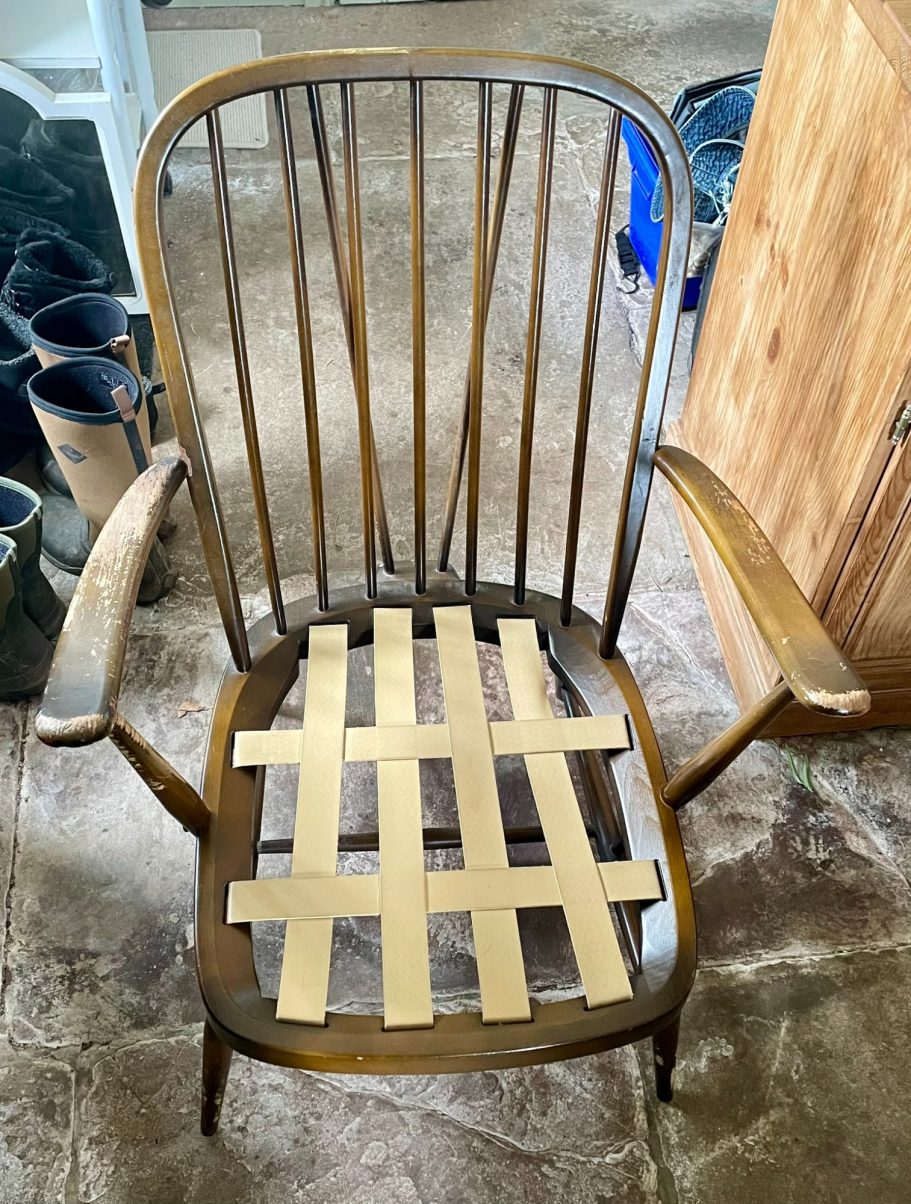 Ercol chair at the start A wooden chair with a woven seat made of light-coloured strips.