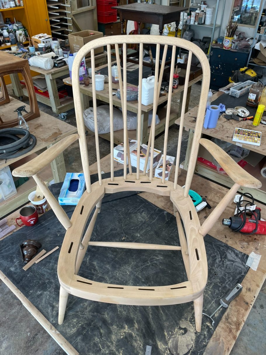 Finally stripped! A wooden chair frame with wide armrests and a slatted backrest in a workshop.